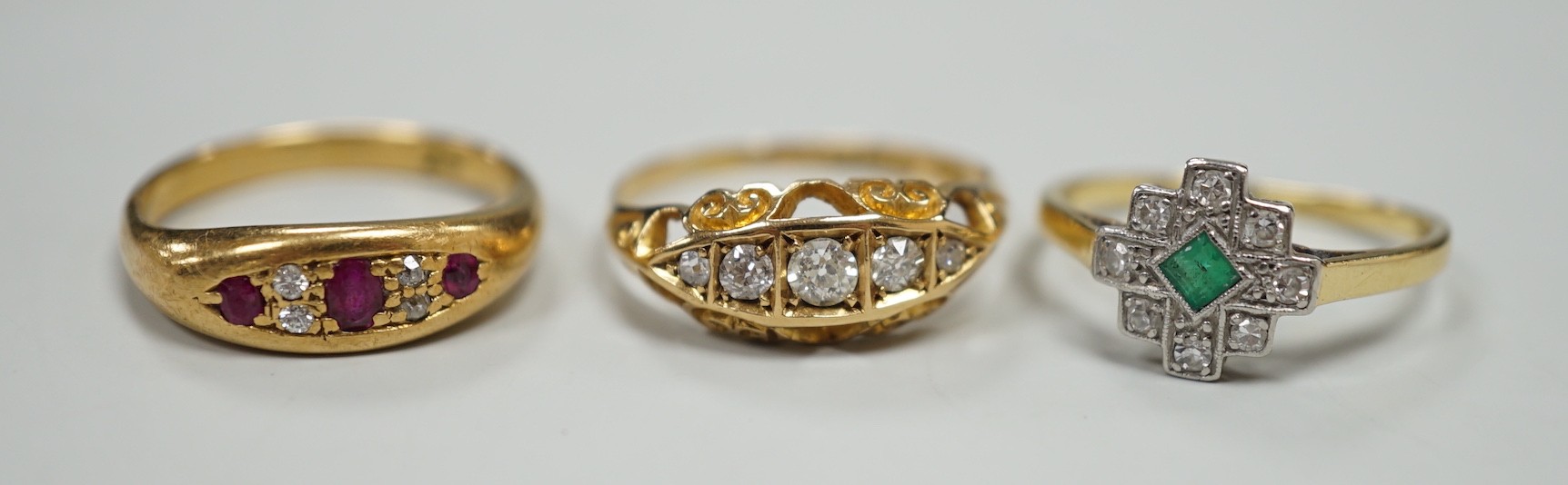 Three early 20th century 18ct and gem set rings, including ruby and diamond chip, size O, graduated five stone diamond, size P and an emerald and diamond cluster, size M, gross weight 10 grams.
